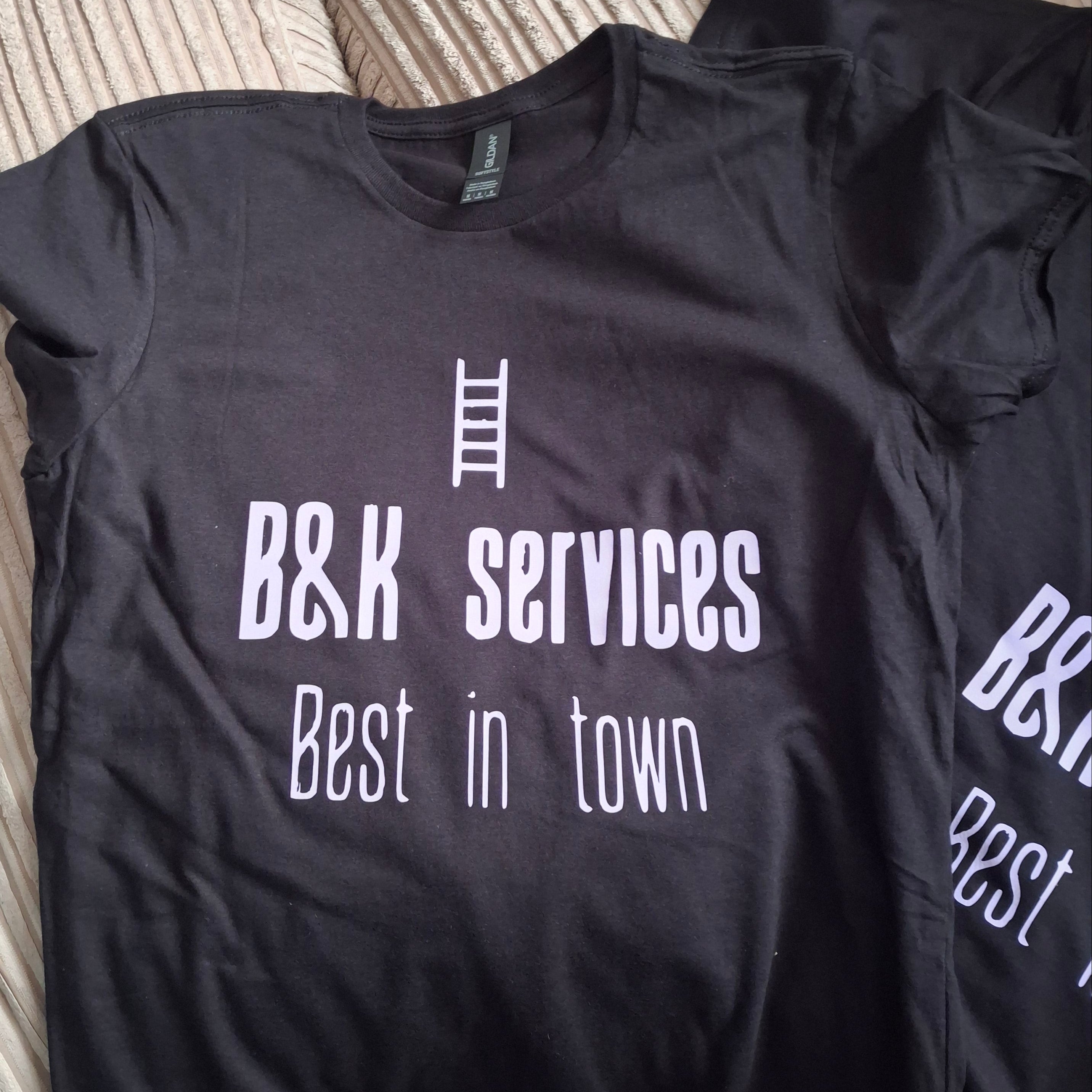 A black short-sleeve t-shirt laid flat on a ribbed beige couch, featuring white printed text that reads 'B&K SERVICES Best in town' with a small white icon.