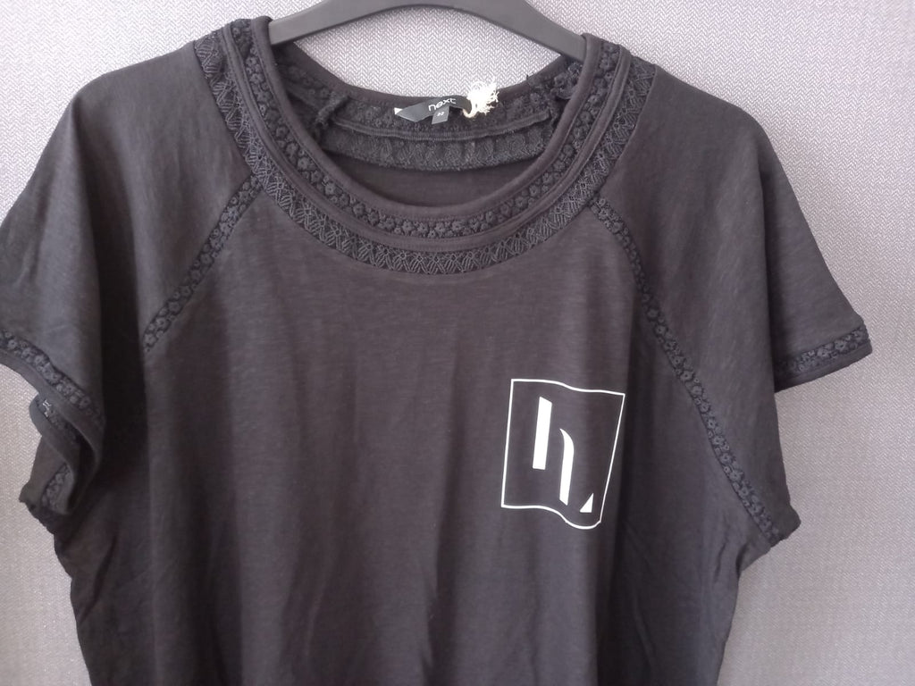 A dark gray short-sleeve raglan t-shirt with lace trim around the crew neck and sleeves, featuring a white graphic logo on the left chest, hanging on a gray hanger against a light gray textured wall.