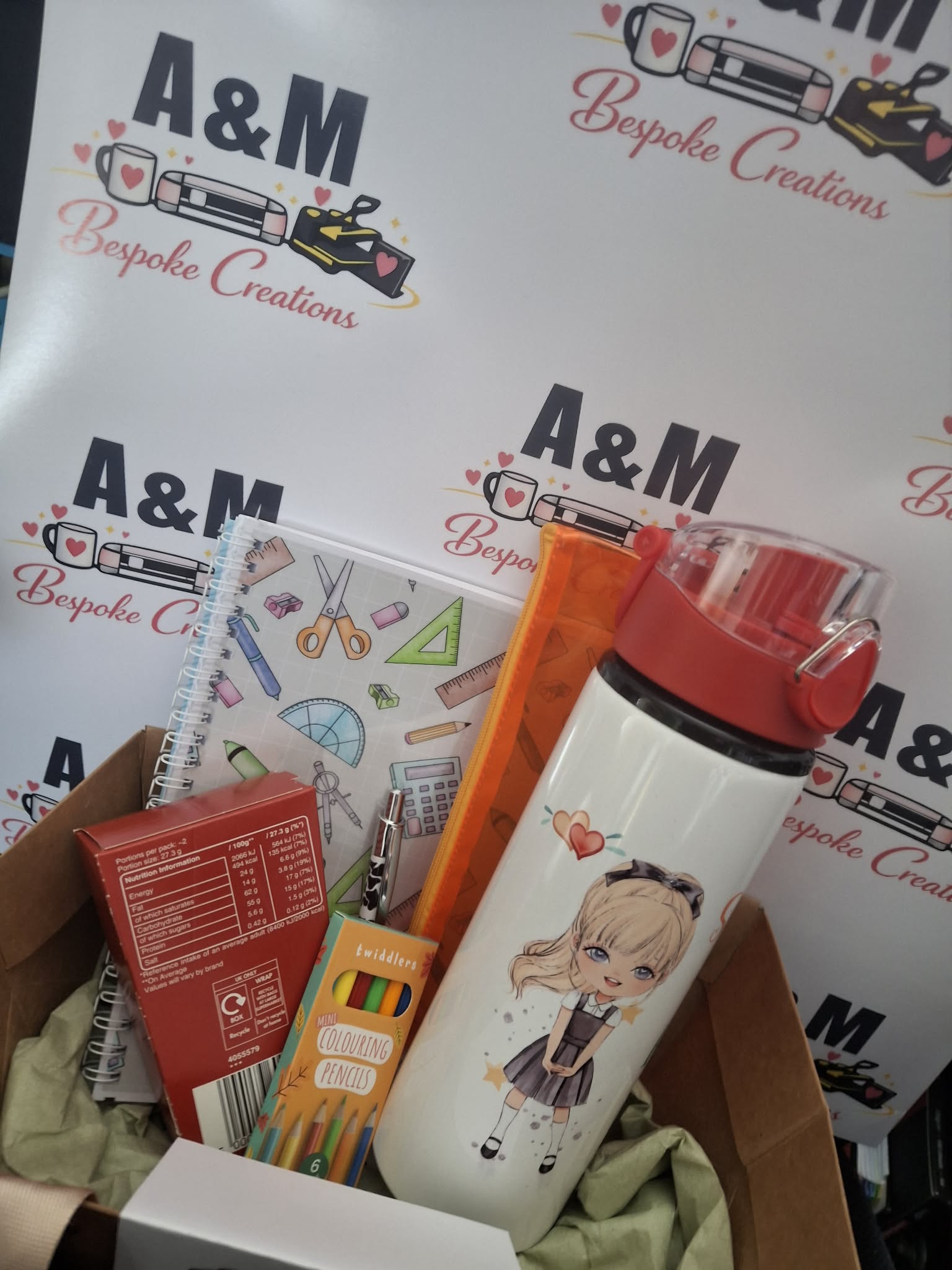 A curated stationery and lifestyle gift box featuring a white insulated water bottle with a red lid and anime character print, alongside notebooks, a treat box, and a pencil case, set against a branded A&M Bespoke Creations backdrop.
