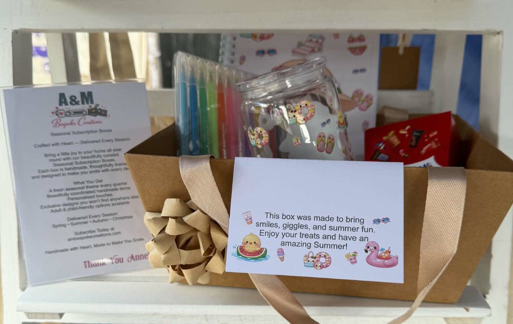 A curated gift box set featuring a brown cardboard box tied with a beige ribbon, containing a clear jar with cartoon stickers, colorful pens, a printed instruction card, and a welcome message card. A white sign on the left reads 'A&M Happy Makes'.