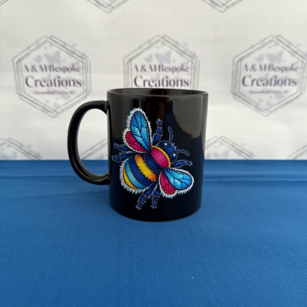 A striking black mug featuring a vibrant faux‑denim patchwork bee design. Bright, bold, and perfect for anyone who loves unique, colourful artwork on their everyday mug.