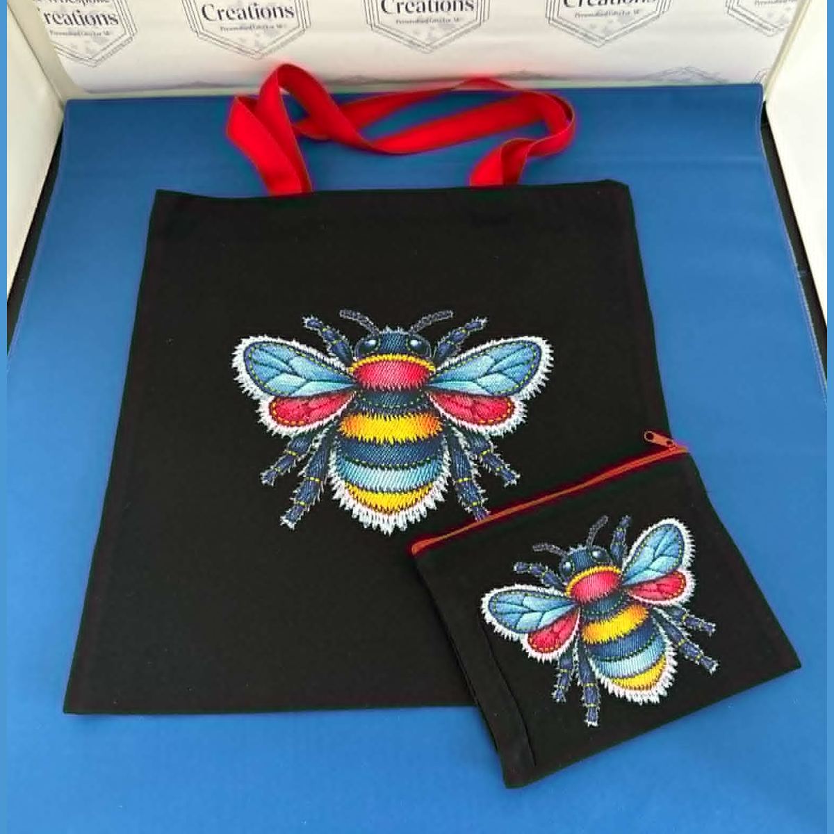 A beautiful black tote bag with bright coloured handles, paired with a matching zippered pouch — both featuring a vibrant faux‑denim patchwork bee design. Cute, bold, and perfect for everyday use or gifting.